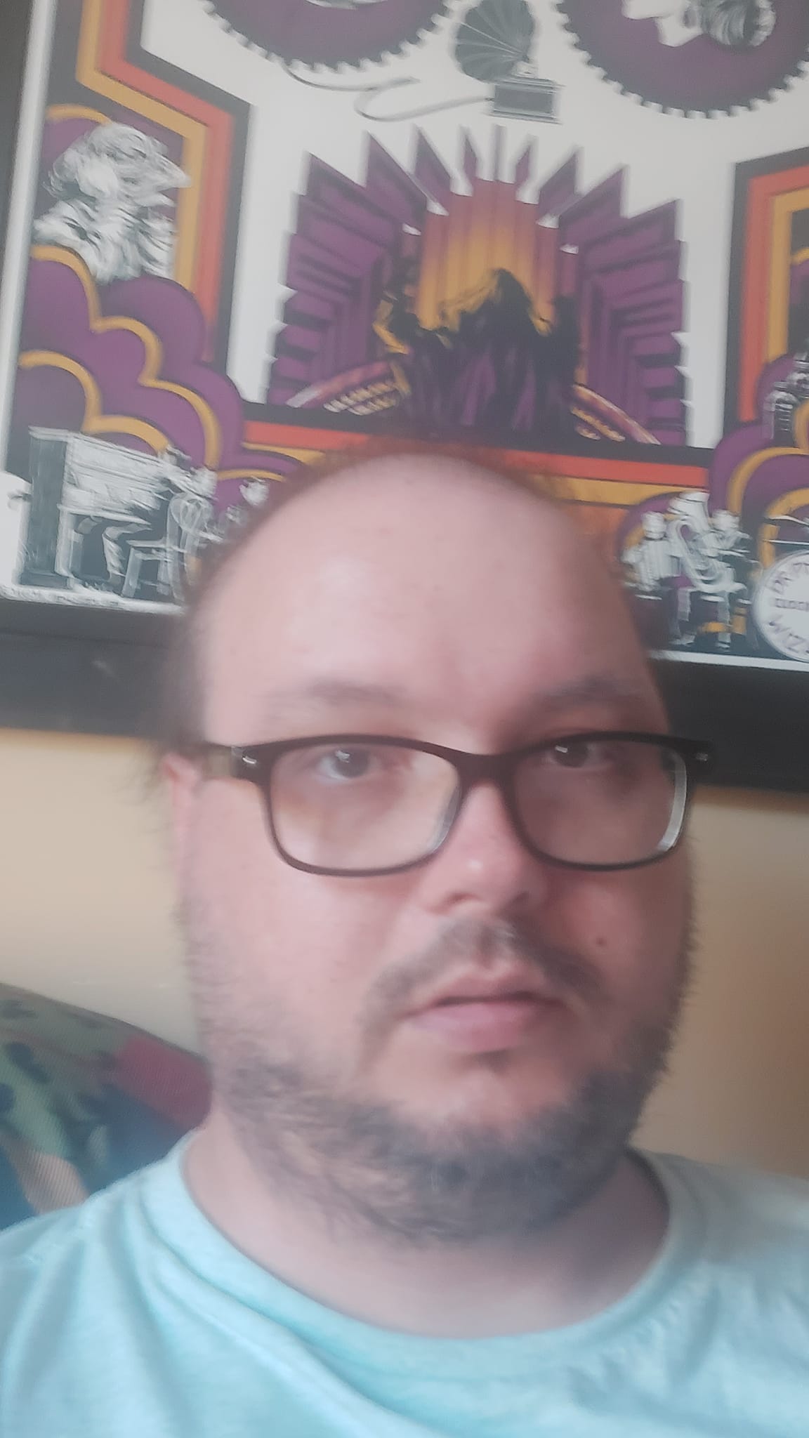 A man wearing a blue shirt sits in front of a poster for the film The Abominable Doctor Phibes, he looks dazed and tired